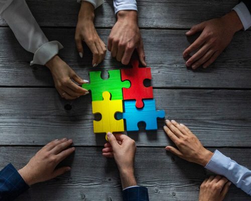 Business people team sitting around meeting table and assembling color jigsaw puzzle pieces unity cooperation ideas concept